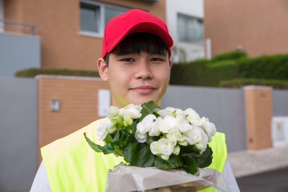 Close-up of a floral arrangement being handed over as a floral gift, featuring a bouquet of white and cream tulips wrapped in light pink paper, held by a person with a blurred woman in a white shirt a