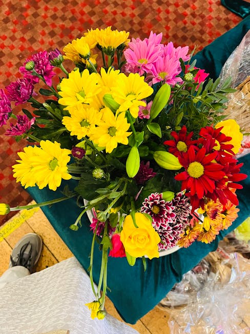 A vibrant bouquet featuring a mix of fresh flowers arranged in a lush, rounded style. Bright yellow chrysanthemums with layered petals are prominent, complemented by deep red daisies with yellow cente