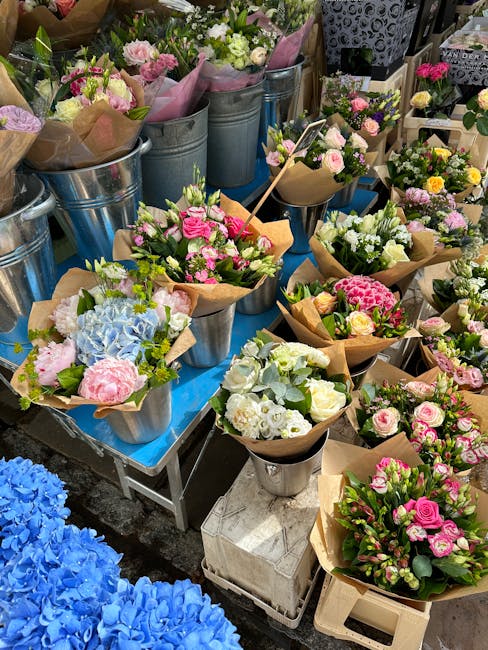 An outdoor display of vibrant floral arrangements on a table, featuring a variety of freshly cut flowers including pink roses, white roses, light green and white hydrangeas, and pink carnations, all w
